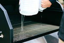 A person pours water from a large jug onto the grates of an empty Myron Mixon BARQ-H2O Pellet Smoker by Myron Mixon Smokers, possibly cleaning it before a competition-style BBQ.