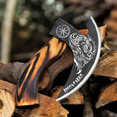 The Texan Knives Custom Hand-Engraved Pizza Axe features an 8-inch J2 steel blade with skull and rune engravings, plus a curved wooden handle. Shown resting on stacked firewood outdoors.