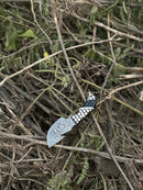 The Texan Knives Exquisite Custom Handmade Damascus Steel Guthook Skinning Knife features a unique resin handle and a 7.5” blade. Pictured outdoors with dry branches and green ferns, it comes complete with a leather sheath.