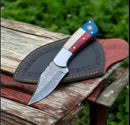 The Texan Knives Custom Handmade Texas Flag Damascus Steel Hunting Knife with an exotic wood-bone handle rests on a black leather sheath atop a weathered wooden surface outdoors.