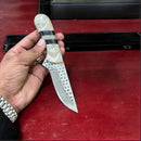 A hand holds the Texan Knives Premium Handcrafted Cowboy Knife, featuring an 8" rasp blade and a resin handle with black and white stripes, set against a red background.
