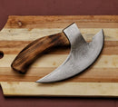 The Texan Knives Axe Pizza Cutter – Custom Hand-Engraved J2 Steel Blade with Wooden Handle rests on a striped wooden cutting board against a brown background.