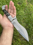 A hand holds the Texan Knives Custom Handmade 12" Damascus Steel Hunting Knife with a buffalo horn handle and Damascus steel bolster, photographed outdoors on green grass. Includes leather sheath.
