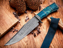A Texan Knives Custom Handmade 13" Damascus Steel Confederate Civil War Bowie Knife with a camel bone handle and leather sheath is displayed on a wooden surface, surrounded by wooden blocks, black cloth, and pinecones.