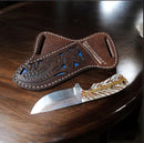 The Texan Knives Handmade Cowboy Belt Knife, featuring a rasp steel blade and patterned pine cone handle, sits next to its floral-tooled brown leather sheath on a dark wooden surface.