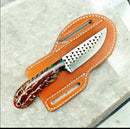 The Texan Knives Handcrafted Cowboy Knife Set features a patterned blade and multicolored handle, resting on a brown leather sheath—an eye-catching piece from Texan Knives, perfect for any cowboy collection.
