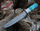 The Texan Knives Custom Handmade 13" Damascus Steel Civil War Bowie Knife features a patterned blade, a blue and white camel bone handle, and comes with a red leather sheath with button clasp. The knife is displayed resting on wood.