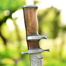 Close-up of the Texan Knives Custom Handmade 13" Damascus Steel Civil War Bowie Knife, featuring a polished rosewood handle and detailed guard, set against a blurred green outdoor background. Includes leather sheath.