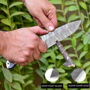 A person carves a branch with the Texan Knives Custom Handmade 9" Damascus Steel Hunting Knife, featuring a drop point blade, razor sharp edge, and durable G10 handle; insets show blade features. Leafy green plants are in the background.