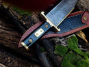 The Texan Knives 13-Inch Damascus Steel Cowboy Bowie Knife features a patterned blade and ornate black and brass buffalo horn handle, shown on its leather sheath atop mossy logs—an ideal gift for knife enthusiasts.