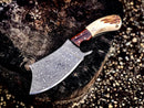 The Texan Knives Handmade Damascus Steel Cleaver Knife features an antler horn handle, rosewood bolster, and comes with a leather sheath—shown outdoors on a tree stump.
