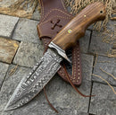 The Texan Knives 🔥 Handmade Damascus Steel Hunting Knife features a patterned blade, rosewood handle, and Damascus guard, resting on its brown leather sheath with decorative stitching atop gray stone tiles.