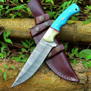 The Texan Knives Custom Handmade Damascus Steel Hunting Knife features a 10-inch blade and a resin handle. It comes with a leather sheath, displayed on tree logs among green leaves.