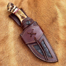 The Texan Knives Custom Handmade Damascus Skinning Knife features a 4.5" blade, a carved sheep horn handle, and comes with a detailed brown leather sheath with black inlay, decorative stitching, and an attachment loop.