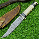 The Texan Knives Handmade Western Boulder Colorado Knife features an 11" Damascus steel blade, a camel bone handle with brass accents, and a custom leather sheath—an eye-catching display on artificial grass.