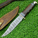 The Texan Knives Western Boulder Colorado Knife features a 13” handmade Damascus steel blade, a rosewood handle, and brass accents, shown resting on grass beside its brown leather sheath with yellow stitching.