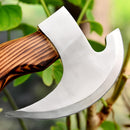 A close-up of the Texan Knives Forged Pizza Cutter, featuring a custom handmade J2 steel blade and handcrafted wood handle, held outdoors near green leaves and branches.