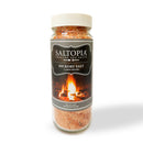 A clear jar of SALTOPIA Infused Sea Salts Hickory Salt: CABIN FEVER, topped with a beige lid, displays a campfire label. The reddish-brown smoked salt inside is the perfect BBQ seasoning.