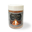 A clear jar with a white lid contains SALTOPIA Infused Sea Salts' Best Grilling Salts: Thrills for the Grill. The black label features a campfire and is perfect for BBQ seasoning or smoked sea salt grilling.