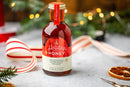A glass bottle of Honey Truck Co. Holiday Honey® – Christmas Spiced Honey featuring a red label with ingredients including cinnamon, clove, and nutmeg.