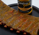 A rack of ribs coated in mustard-based Carolina Gold BBQ sauce next to a bottle of Gourmet Carolina Gold Mix-and-Match 6-Pack of Gourmet Carolina Gold BBQ Sauces.