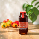 A jar of Honey Truck Co Raw Datil Pepper Infused Honey rests on a wooden table, framed by vibrant datil peppers and a softly blurred green plant in the background. This distinctive creation from Honey Truck Co combines raw honey with spicy datil peppers, delivering a perfect balance of sweet heat to any dish.