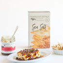 A plate with cheese topped with hot pepper bacon jam is set before a jar of the same jam and a box of Terrapin Ridge Farms Sea Salt Gourmet Crackers. Some crackers from Terrapin Ridge Farms are on the plate and beside the box—a perfect snack for entertaining.