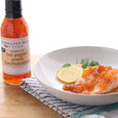 A white plate with chicken topped with orange peach sauce, garnished with lemon and cilantro. Next to it is a Terrapin Ridge Farms Hot Pepper Peach Bourbon Sauce - Quart, a gourmet grilling glaze by Terrapin Ridge Farms.