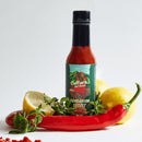 A bottle of Culture Hot Sauce Hungarian Secret by Culture Hot Sauce sits among a red chili pepper, fresh oregano, and two lemons—one whole and one cut in half—against a white background.