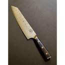 The Spaceman Knives Interstellar Kiritsuke Knife features a wavy Damascus blade and a dark handle with three gold rivets, displayed elegantly on a dark surface.