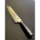 The Spaceman Knives Interstellar Kiritsuke Knife, featuring a Damascus patterned blade and a dark, textured handle, lies on a dark surface, highlighting the elegance and precision of this Spaceman Knives chef’s tool.
