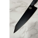 A Spaceman Knives Dark Matter Kiritsuke chef’s knife with its signature angled tip is displayed on a white and gray marble surface.