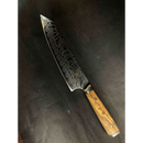 The Spaceman Knives Interstellar Kiritsuke Knife, featuring a patterned AUS-10 steel blade and a light wood handle, rests on a dark, textured surface.