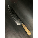 The Spaceman Knives Interstellar Chef Knife features a wavy AUS-10 steel blade and a light wood handle, displayed elegantly on a dark textured surface.