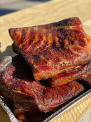 Stack of sweet and smoky smoked pork belly slabs seasoned with BuffalowBBQ Sassy Swine BBQ Rub and cracked black pepper in a metal foil pan.
