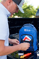 A man reaches into the front pocket of a Blue Coolers 72 Hour Emergency Kit Essential For 1 Person blue backpack sitting on the bed of a truck.