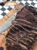 Thinly sliced brisket seasoned with BuffalowBBQ Beef Bark BBQ Rub, featuring a dark, flavorful bark, rests on a wooden cutting board next to a large knife.