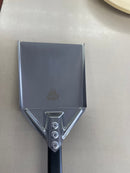 A WPPO Ash Shovel with a black alumina handle, featuring a triangular metal head secured with three rivets, rests on a light countertop. Its sturdy handle offers a secure grip for effortless use. The WPPO LLC Direct logo with flame icon is engraved near the center of the shovel, making it an ideal accessory for any pizza oven.