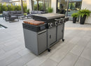 A modern patio showcases a BBQ Boards® 36" Blackstone Griddle Side Cutting Board next to a large gas grill with multiple burners, contemporary seating, and green potted plants enhancing the stylish outdoor space.