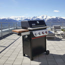 A BBQ Boards® Weber Spirit Reinvented Side Cutting Board sits on a black gas grill on a rooftop patio, with views of snow-capped mountains and a clear blue sky.