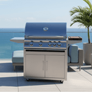 A stainless steel outdoor gas grill with four knobs stands on a patio overlooking the ocean, featuring a BBQ Boards® Blaze Grills LTE or LTE+ Side Cutting Board, surrounded by modern outdoor furniture and potted plants under a clear sky.