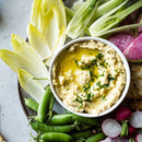Hummus topped with SALTOPIA Infused Sea Salts’ DIVE INTO CHIVES chive salt and olive oil, served with fresh endive, snap peas, celery, watermelon radish slices, and radishes.