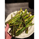 A hand holds a white plate piled with grilled asparagus spears charred with BuffalowBBQ Signature Blend BBQ Rub and a fresh herb aroma.