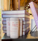 Five tins of World Spice Pink Chili Crisp from World Spice are displayed in front of a stack of books titled 108 Asian Cookies, inside a well-lit store with wooden accents. The vibrant packaging hints at the bold flavors inside—each tin features a unique spice blend starring pink peppercorns, offering a fresh twist on traditional chili crisp.
