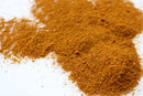 A close-up of a pile of World Spice Japanese Curry powder from World Spice on a white surface, with some of the golden-brown curry powder scattered around.