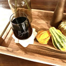 A personalized Wine Decanter - The Diamond stemless wine glass engraved with the name Becca sits on a star-shaped coaster atop a wooden tray decorated with small gourds.