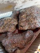 Three pieces of smoked meat featuring dark bark formation and a coarse BuffalowBBQ Beef Bark BBQ Rub in a foil pan.