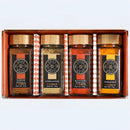 Introducing the Spice Wheel Indian Spice Gift Set by Spice Wheel—a beautifully boxed set featuring four clear jars labeled Garam Masala, Coriander, Kashmiri Powder, and Turmeric. Each jar is adorned with orange and white labels and arranged side by side in elegant brown packaging, making it the perfect collection of essential Indian spices for authentic Indian cooking.
