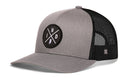 The Haka Hat Indiana Trucker Hat is a gray-black snapback with a curved brim, mesh back, and a round patch on the front showing crossed lines with the letters I, N, D and a small axe graphic.