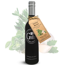 A dark glass bottle from Georgetown Olive Oil Co. displays a tag reading "Italian Herbs White Balsamic." Crafted in Modena, Italy and infused with classic Italian herbs, the vinegar is shown against a backdrop featuring illustrated herbs and garlic.